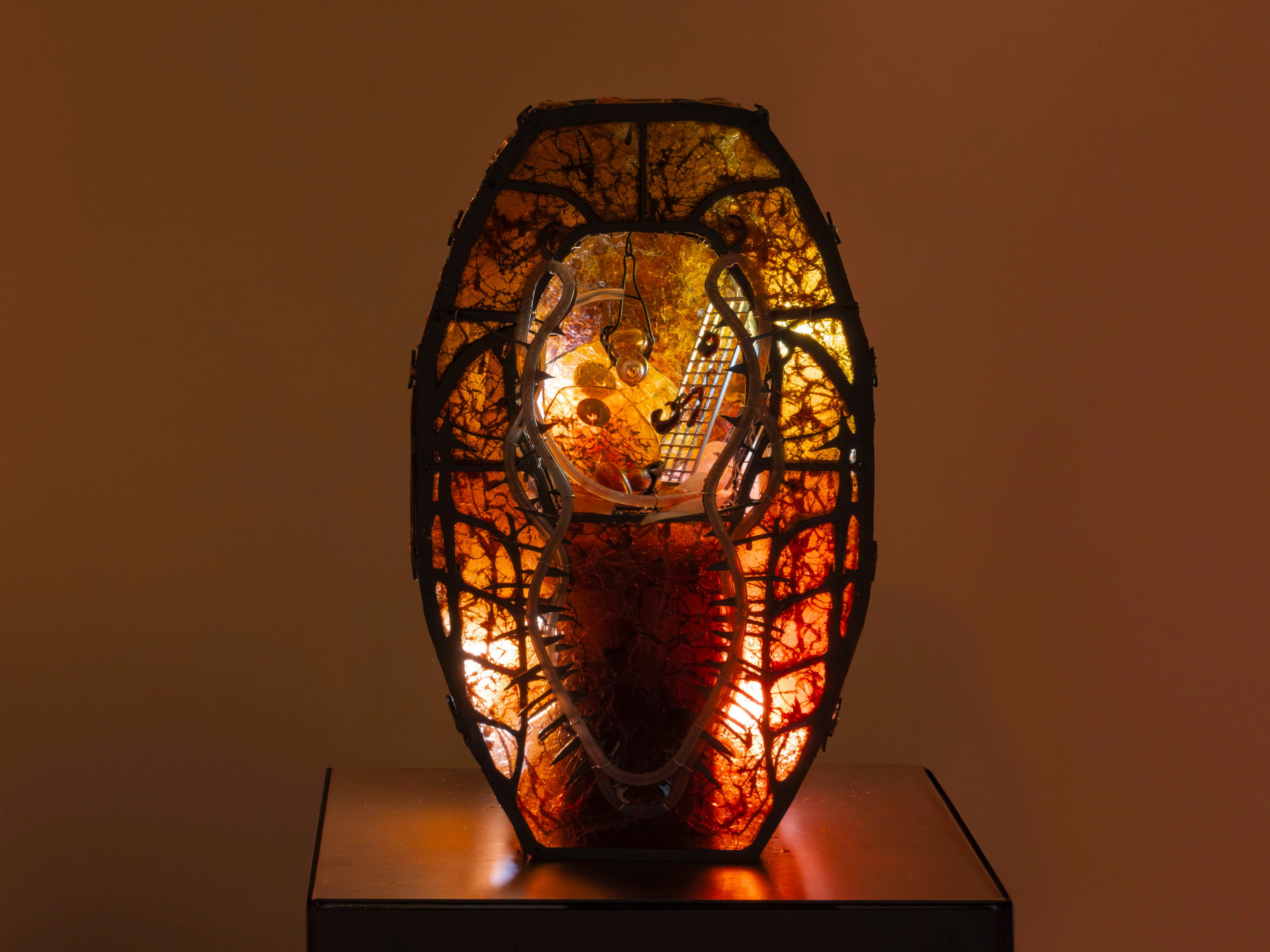 Sculpture by Hazel Brill. Made out of a metal frame and lit from the inside with amber light glowing through resin material. Has an open centre with steam rising from below. Gothic style.