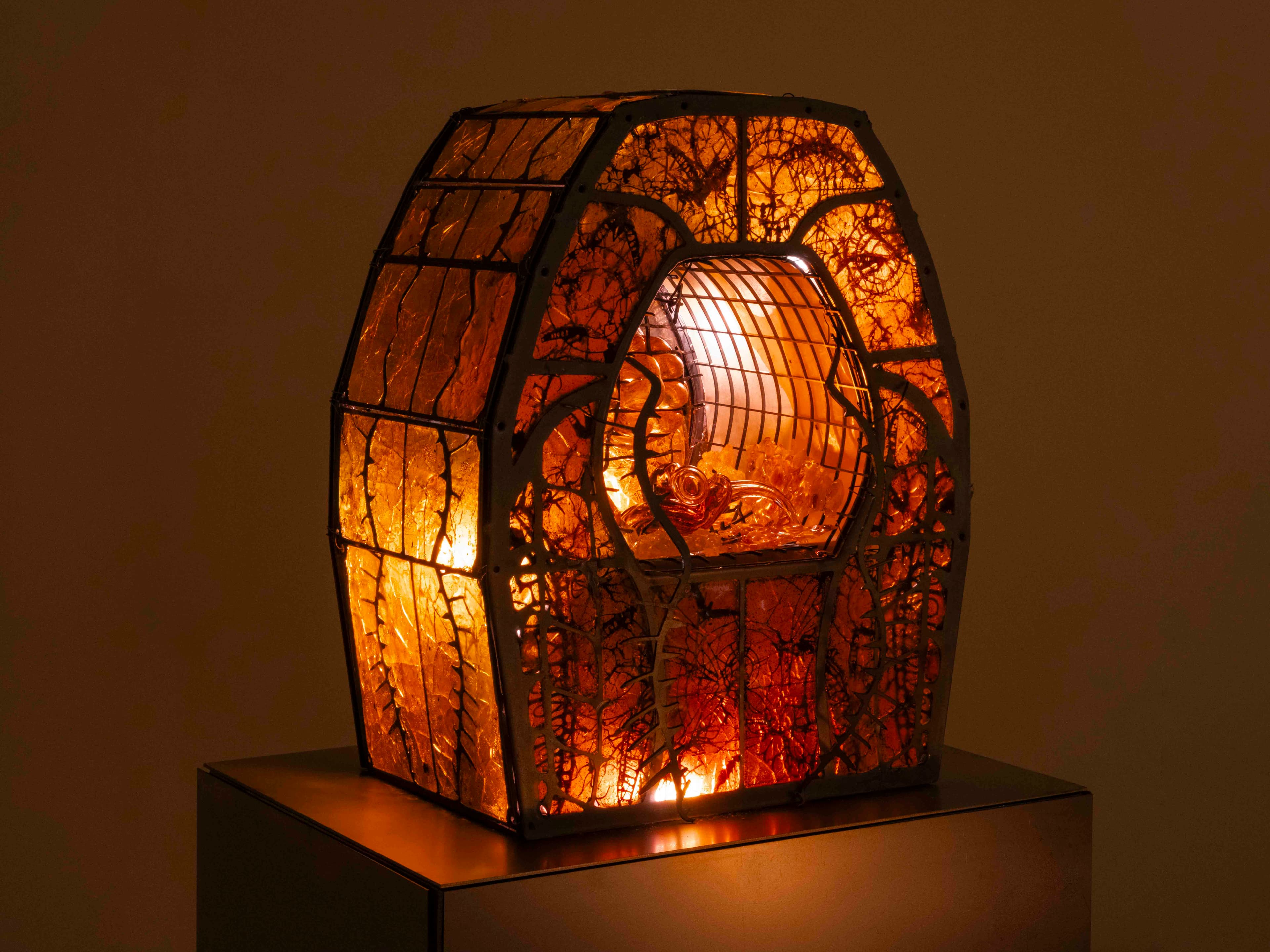 Sculpture by Hazel Brill made in a geometric metal frame with amber coloured orange walls lit in with low lighting and a internal centre with a drip feature. 