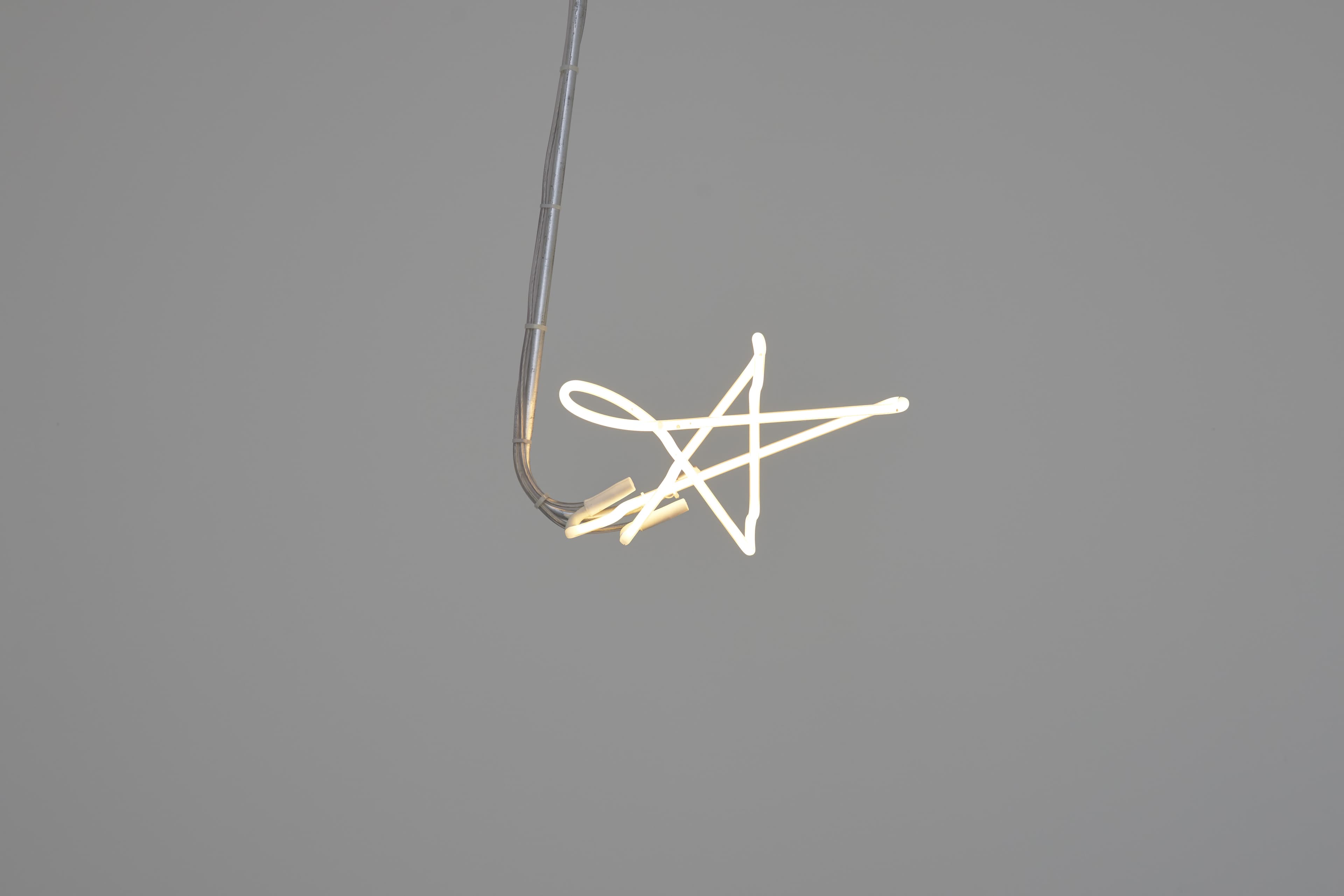 Neon light installation by Max Boyla. White, star shaped neon light suspended on a metal rod from the ceiling.