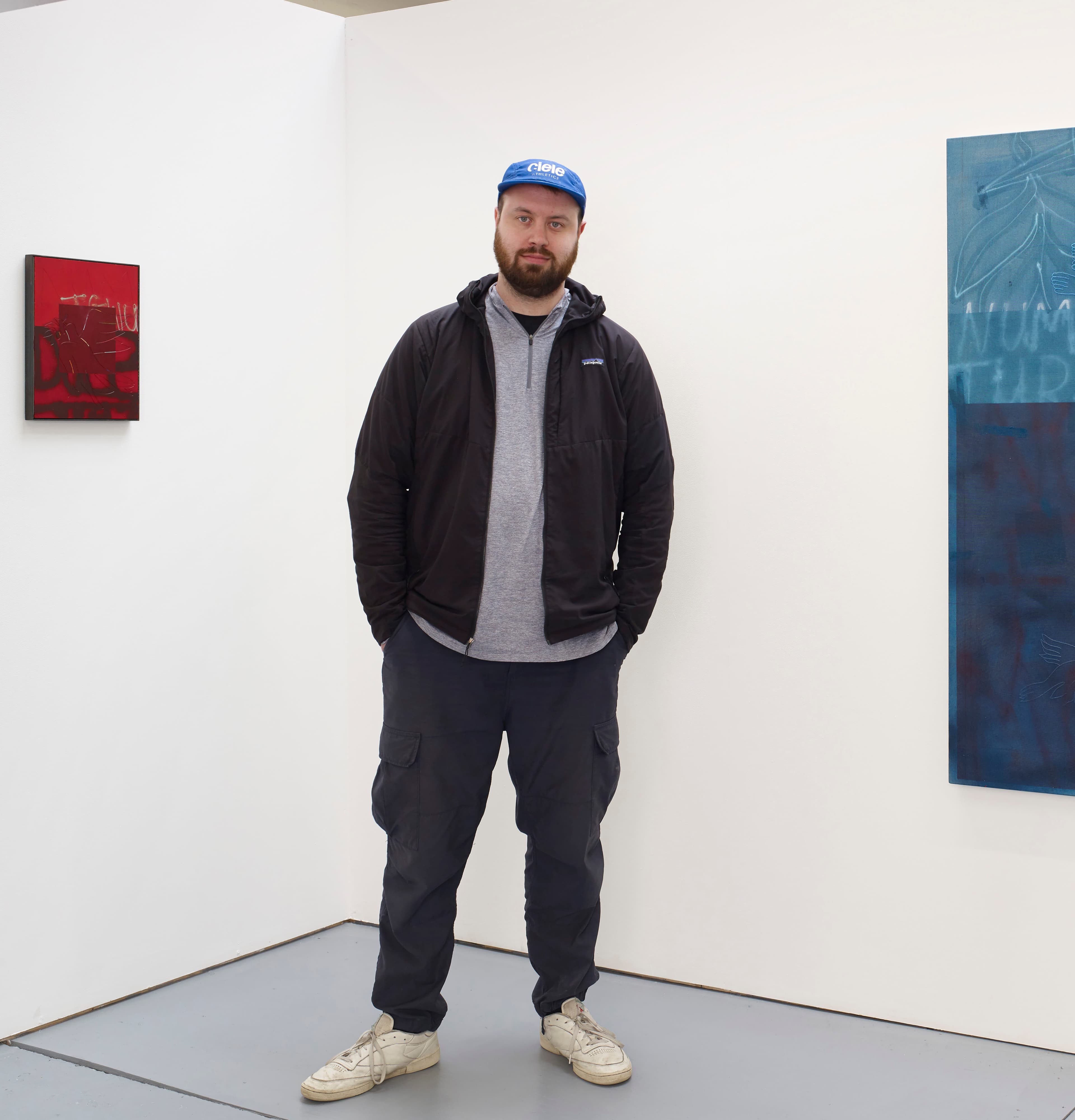 A portrait of Alistair Woods standing in front of two abstract paintings