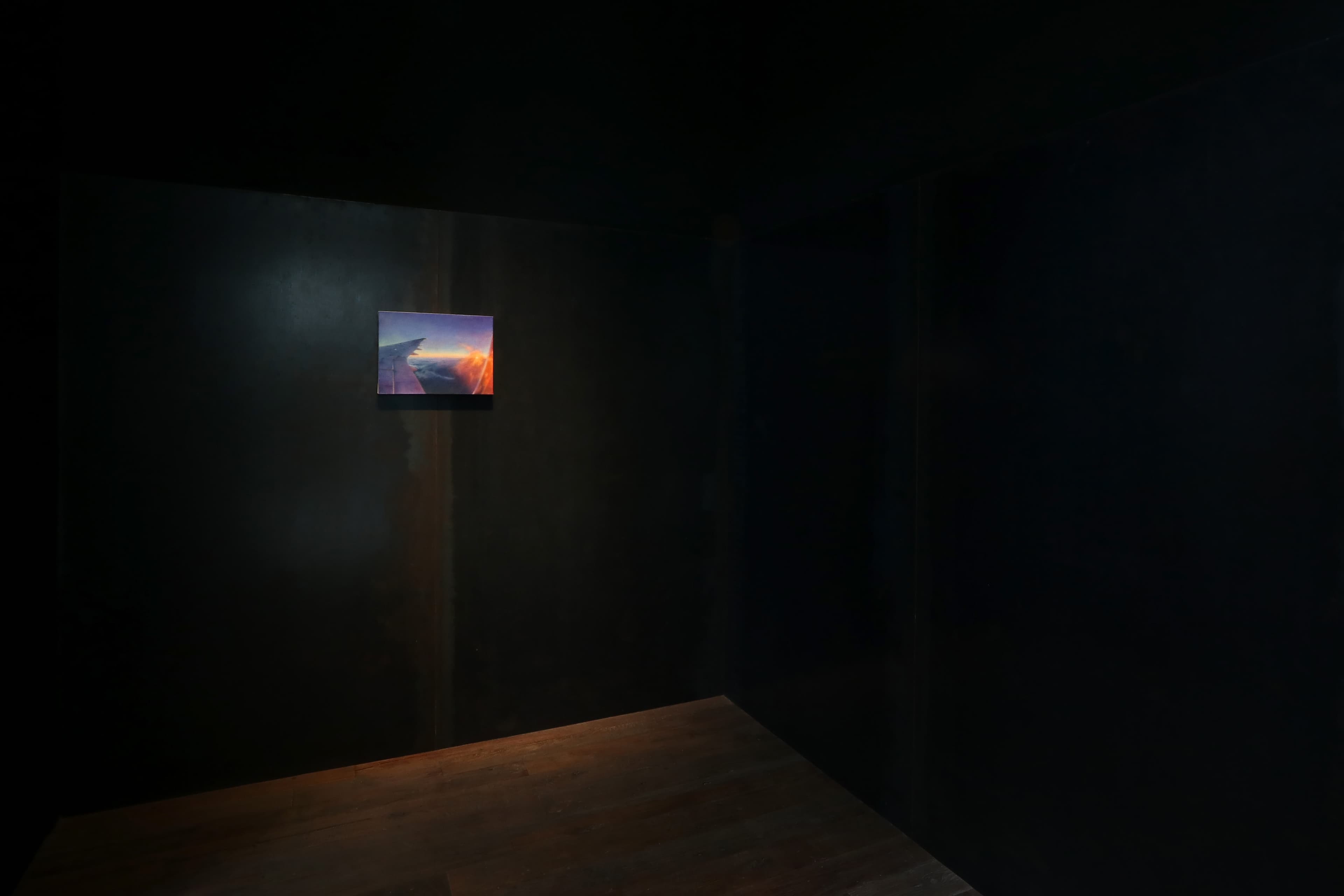 Installation view of a dark room with paintings by James Prapaithong softly spotlit