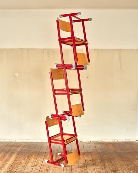 A sculpture by Jacob Dahlgren of a stack of wooden and painted red metal chairs