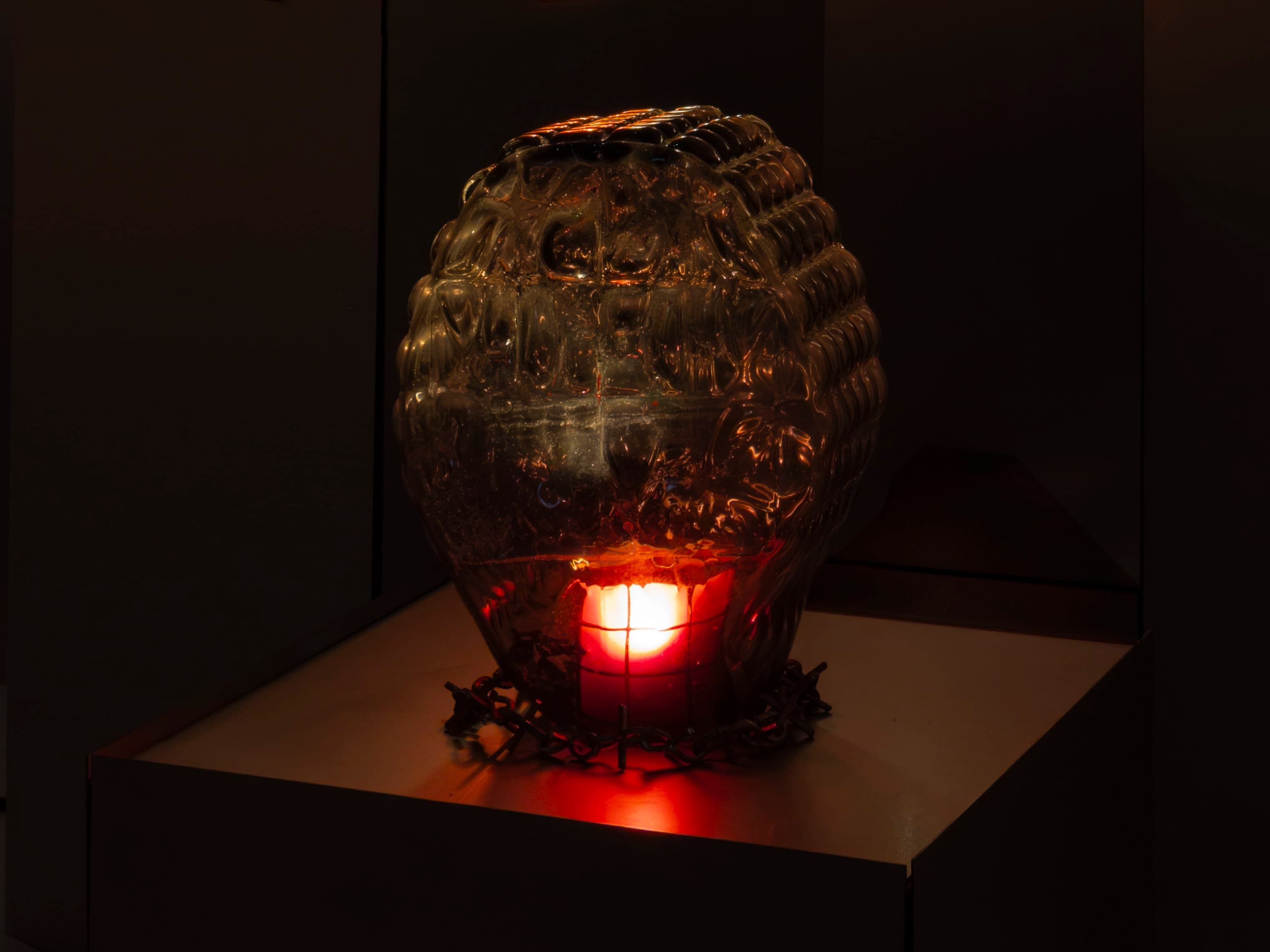 Sculpture by Hazel Brill made from a glass diamond shaped dome with raised circular bobble on the surface lit from the inside with a dim red light bulb.