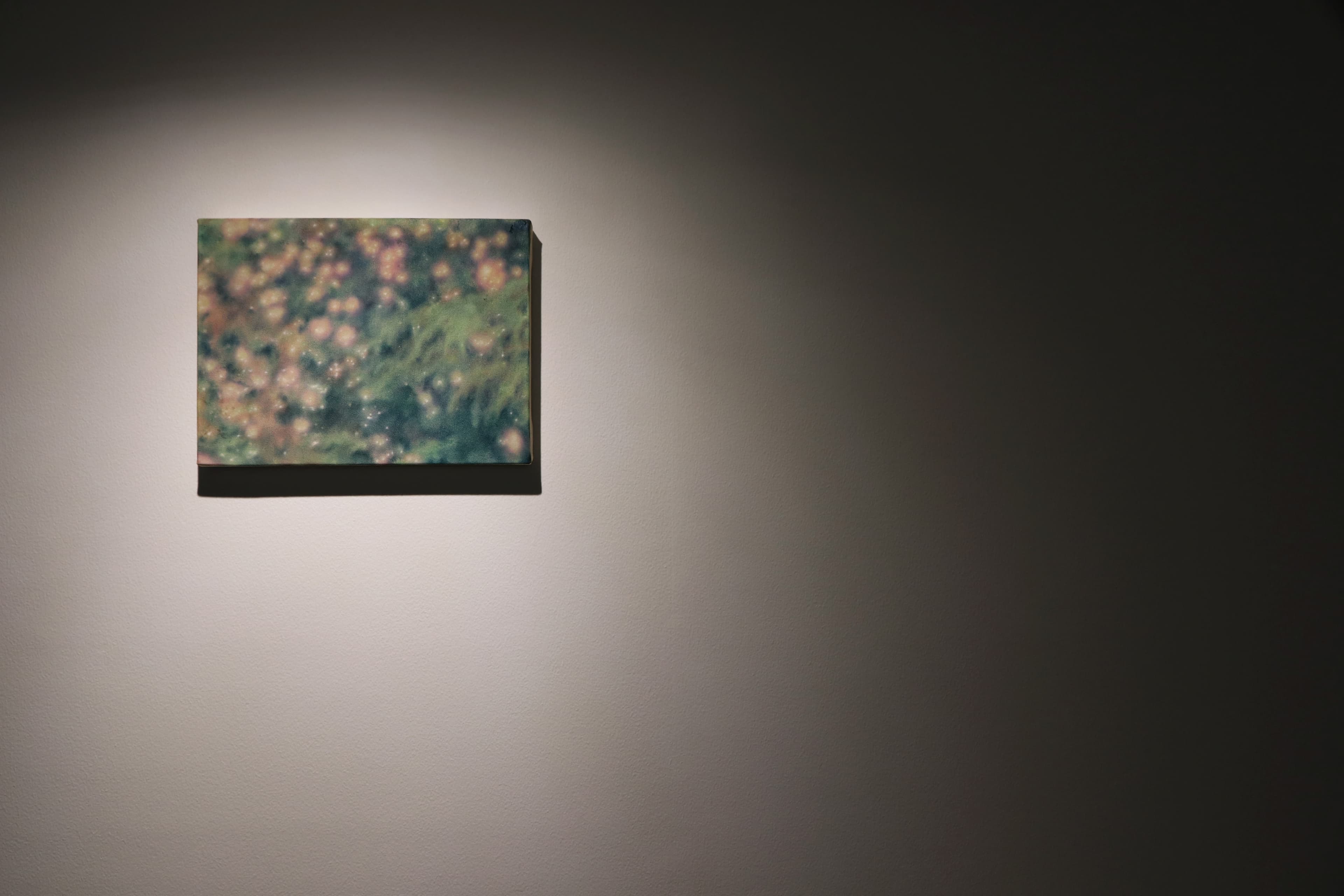 Installation view of a dark room with a painting by James Prapaithong softly spotlit