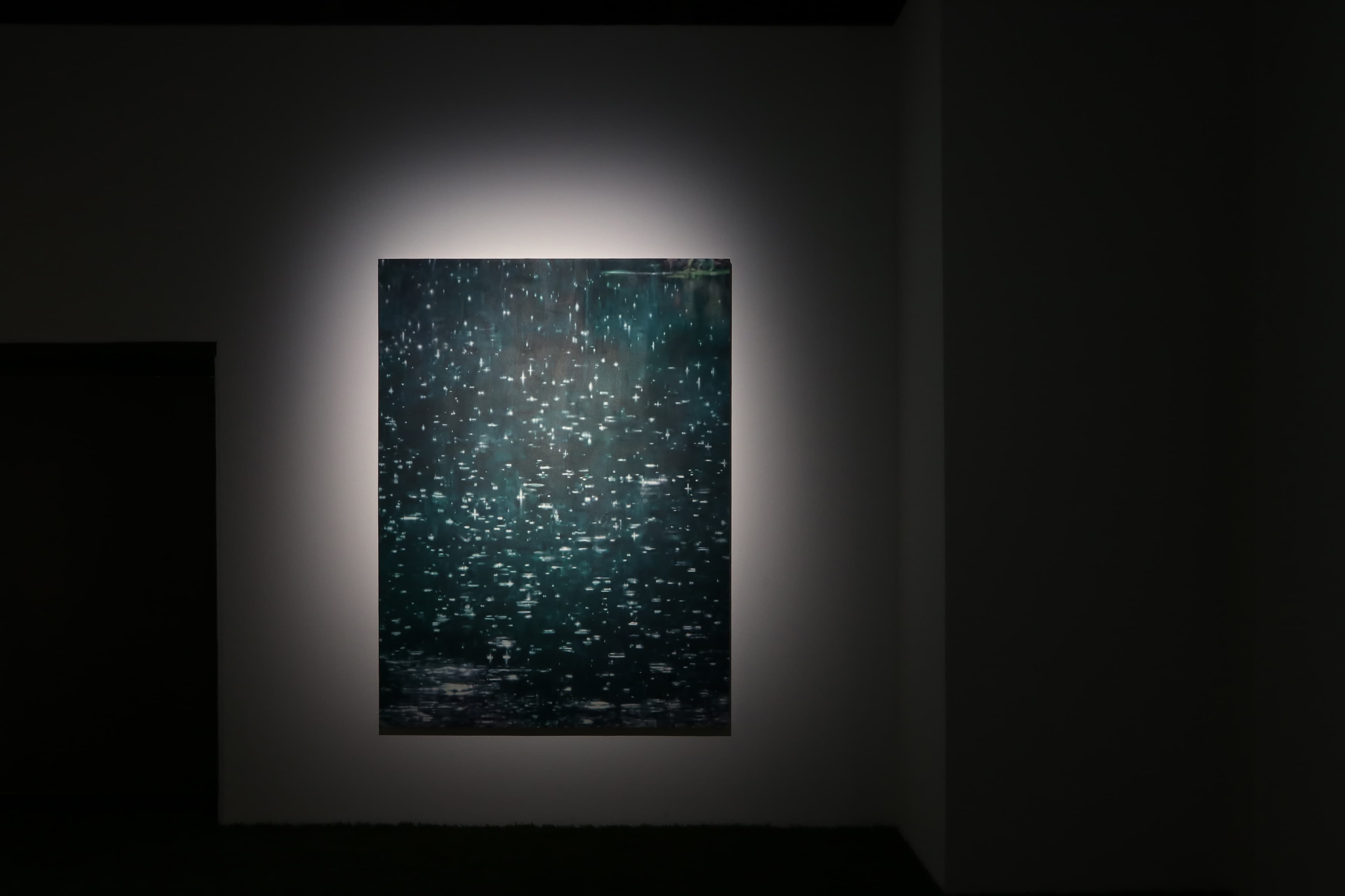 Installation view of a dark room with a painting by James Prapaithong softly spotlit