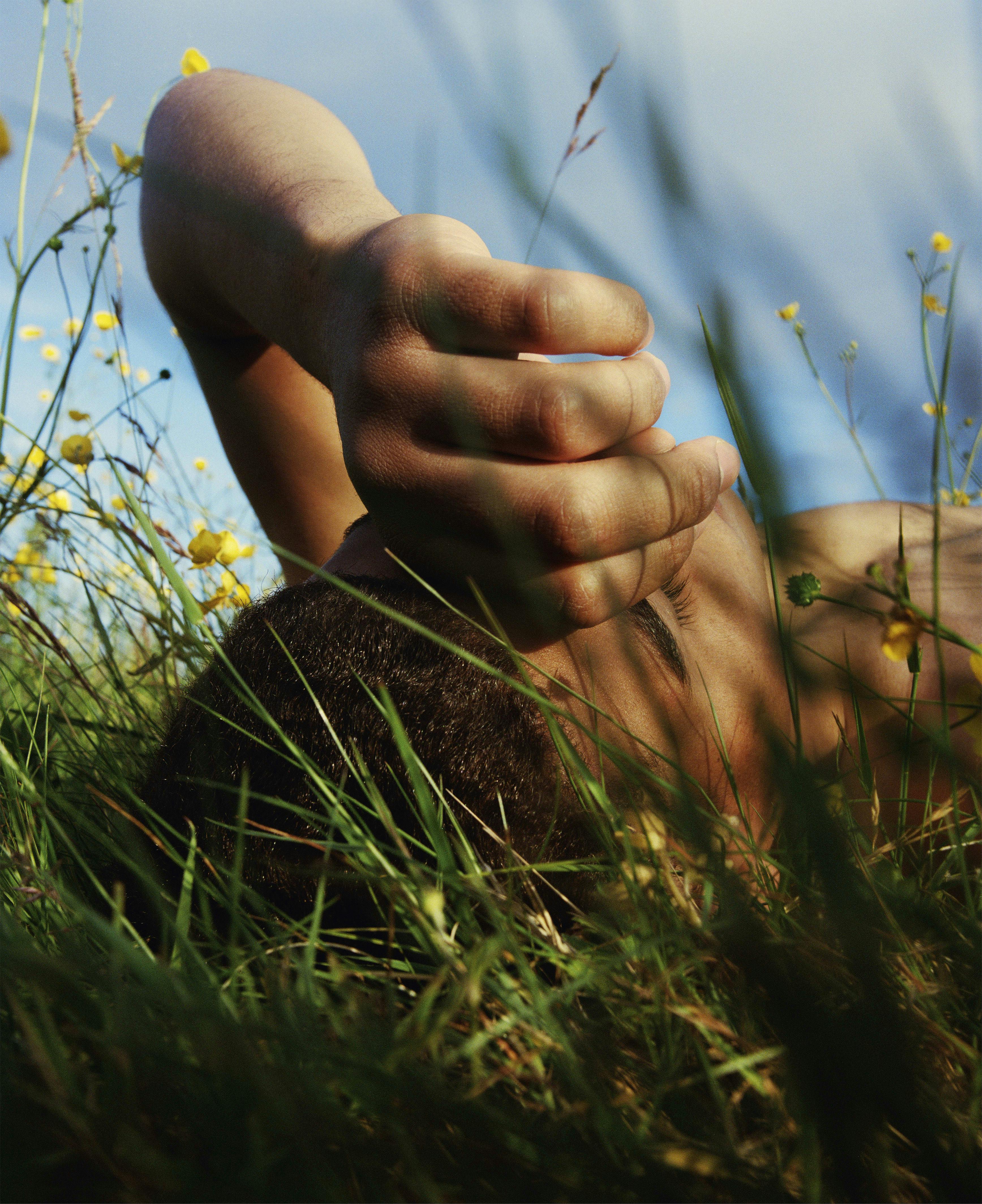 Kuba Ryniewicz' photograph of a boy laying in the grass in the sun, we can see the top of his head and his hand.