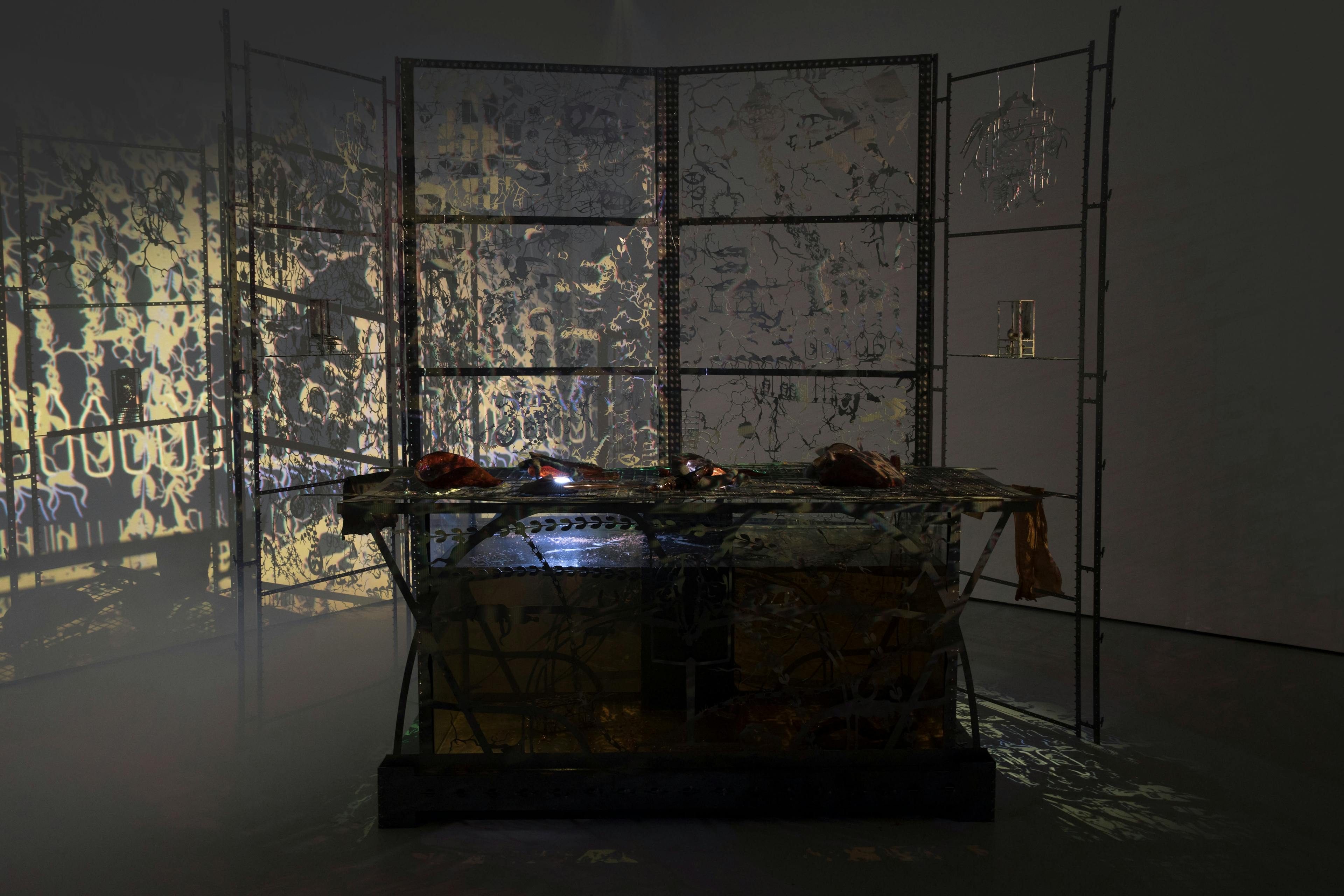 An installation by Hazel Brill including a backlit water tank filled with a dark liquid surrounded by laser cut steel and mouth-blown glass objects