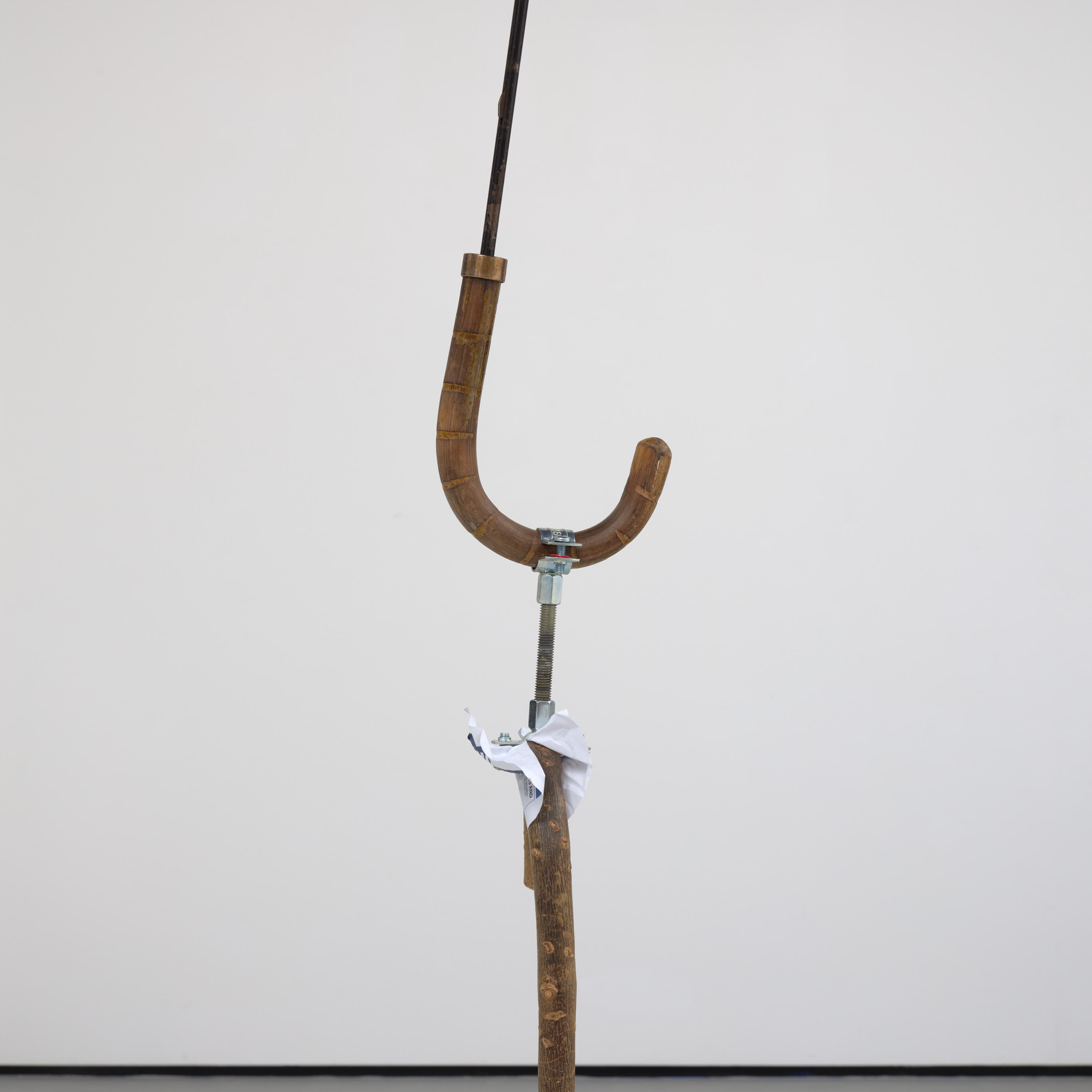 an image of Simeon Barclay's sculpture 'Warrior Falling on Their Feet', 2023 consiting of a Walking stick, umbrella, concrete, betting slip, foot fracture brace walker, bag for life