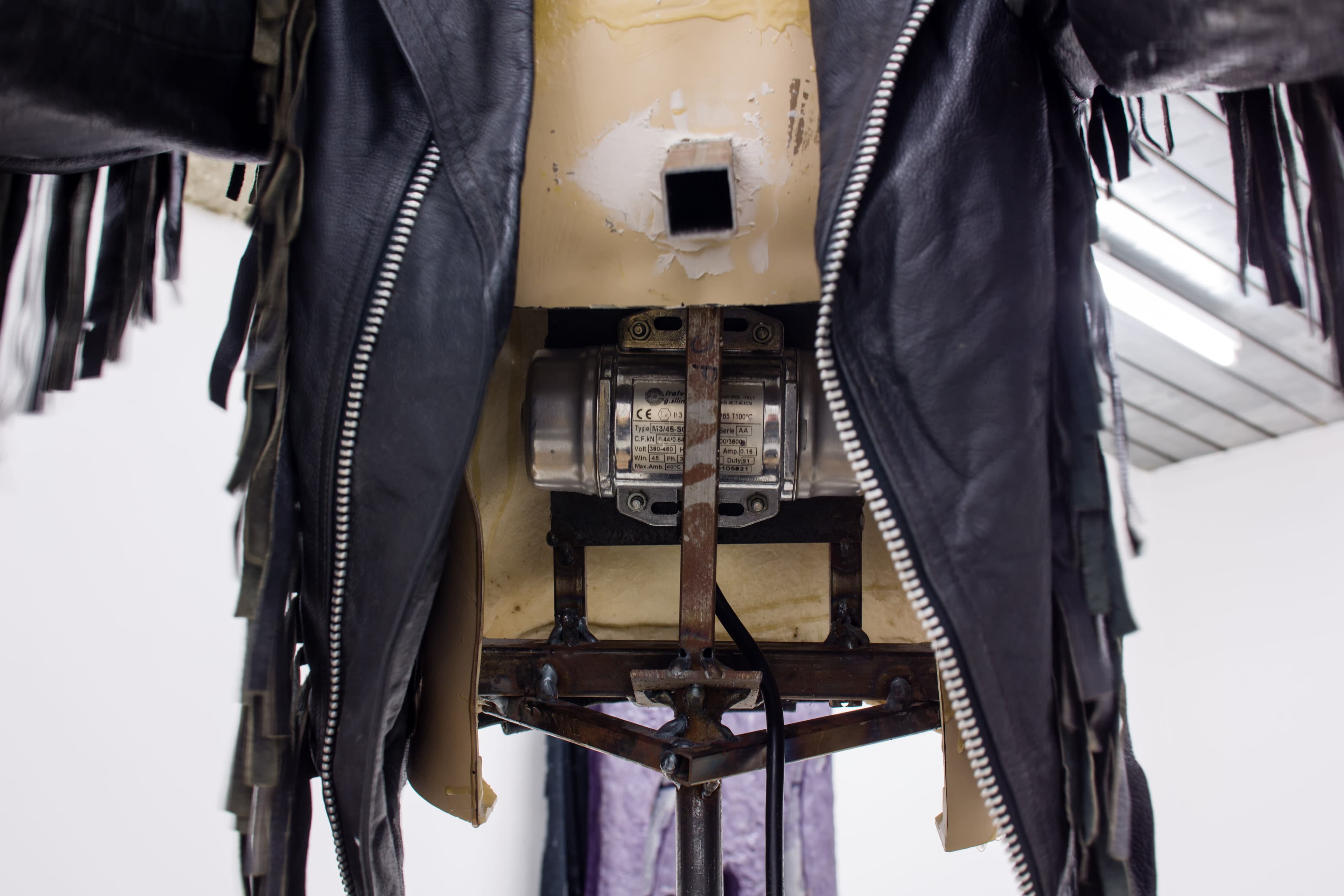 A detail of a sculpture by Mike Pratt of a mannequin torso wearing a leather biker jacked and with a motor inside.