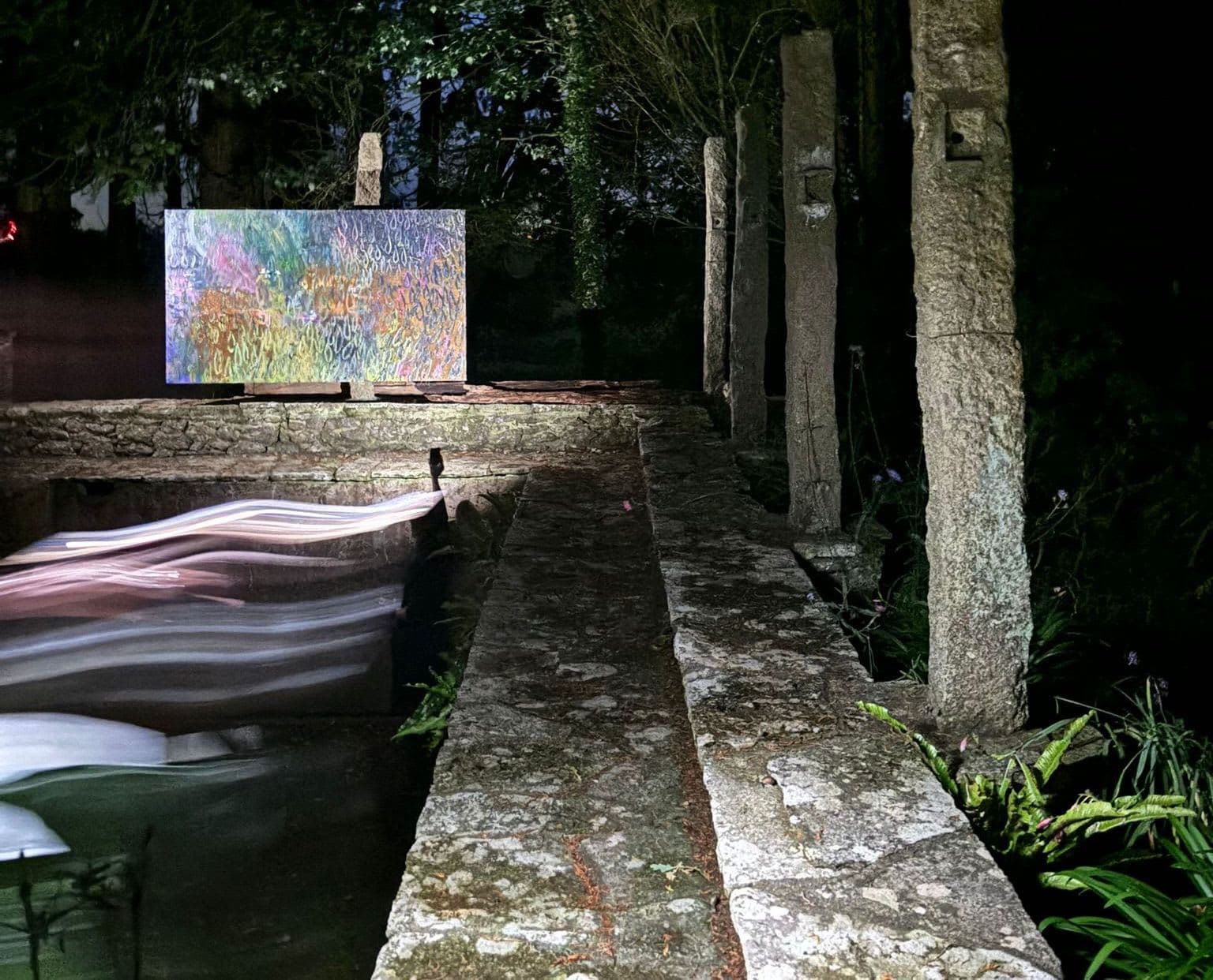 A painting by James Cabaniuk installed outside around a sunken pool in a lush green garden