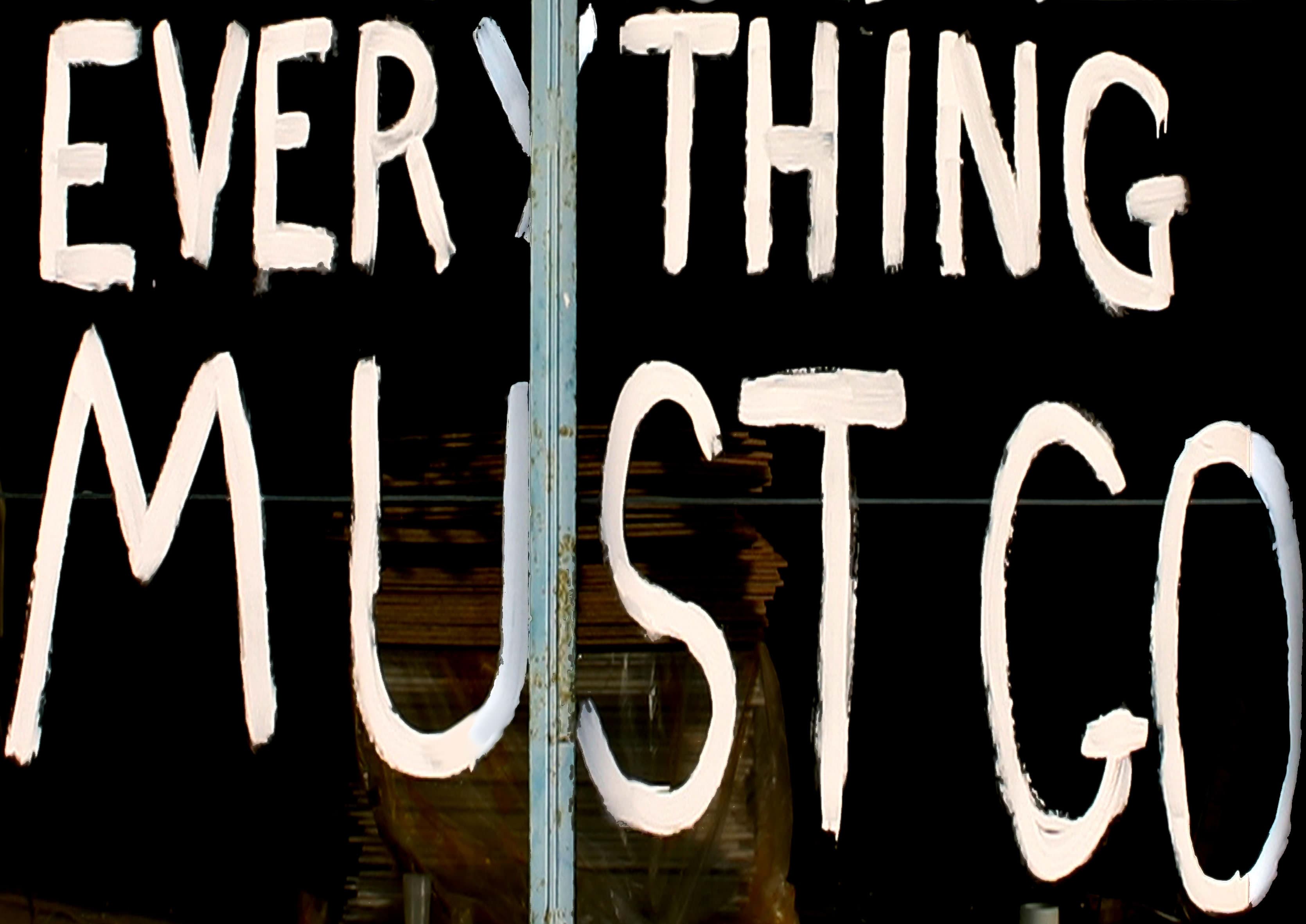 Everything Must Go is written in capital letters in white chalk paint on a darkened shop window. 