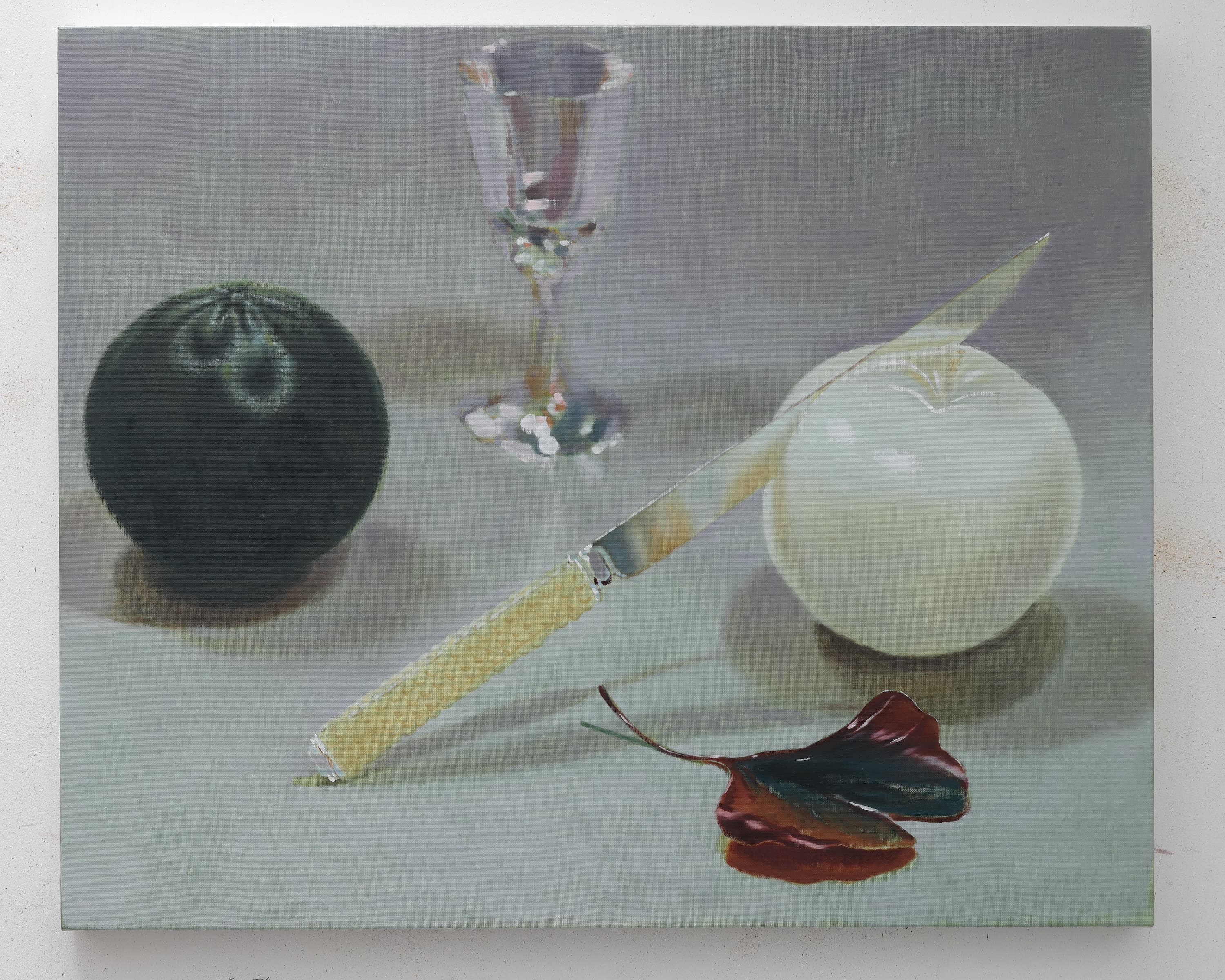 A painting by Robin Megannity of a still life composed of a lime, a glass, a ginko leaf and a white skinned apple being cut into by a knife with a bone handle