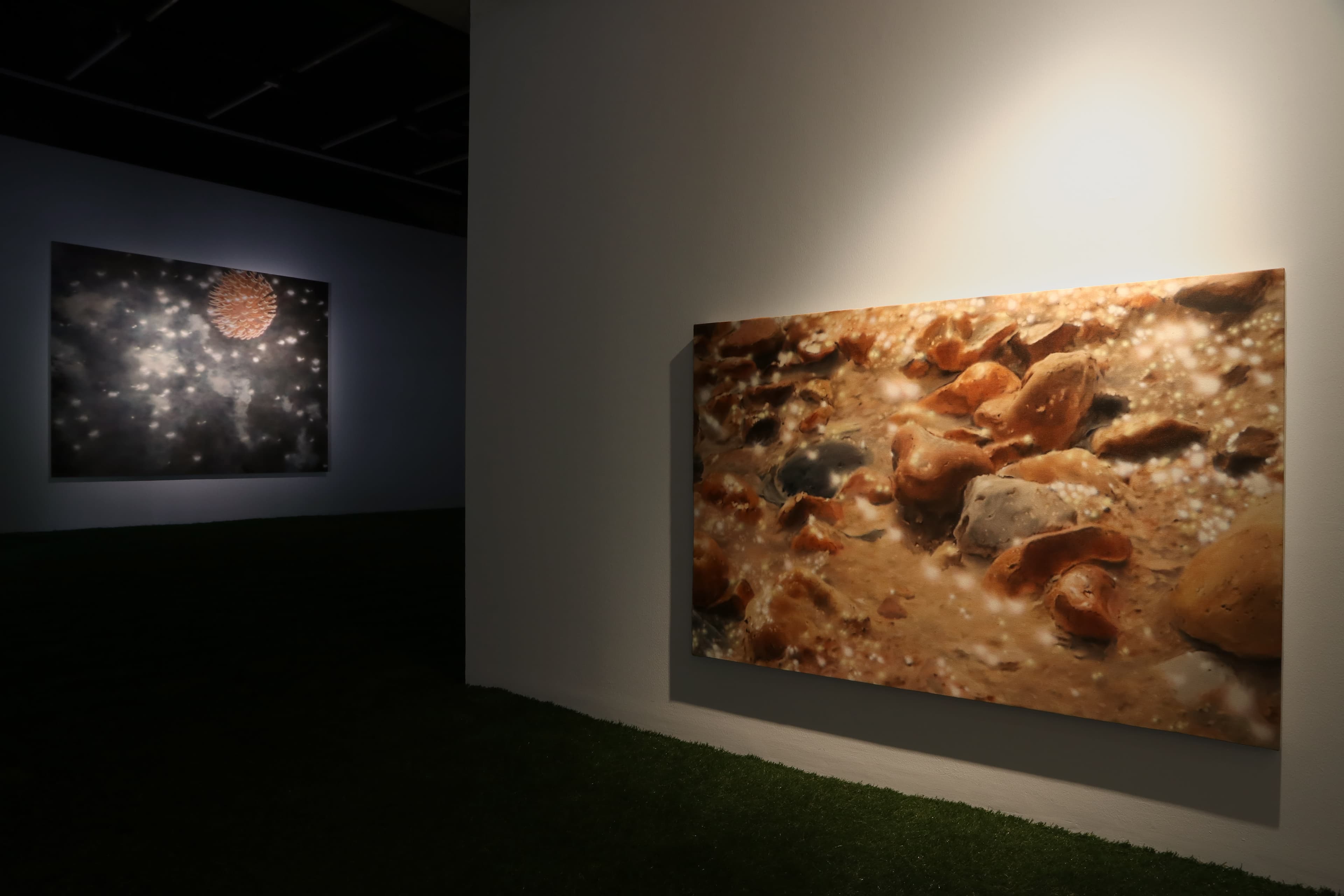 Installation view of a dark room with paintings by James Prapaithong softly spotlit