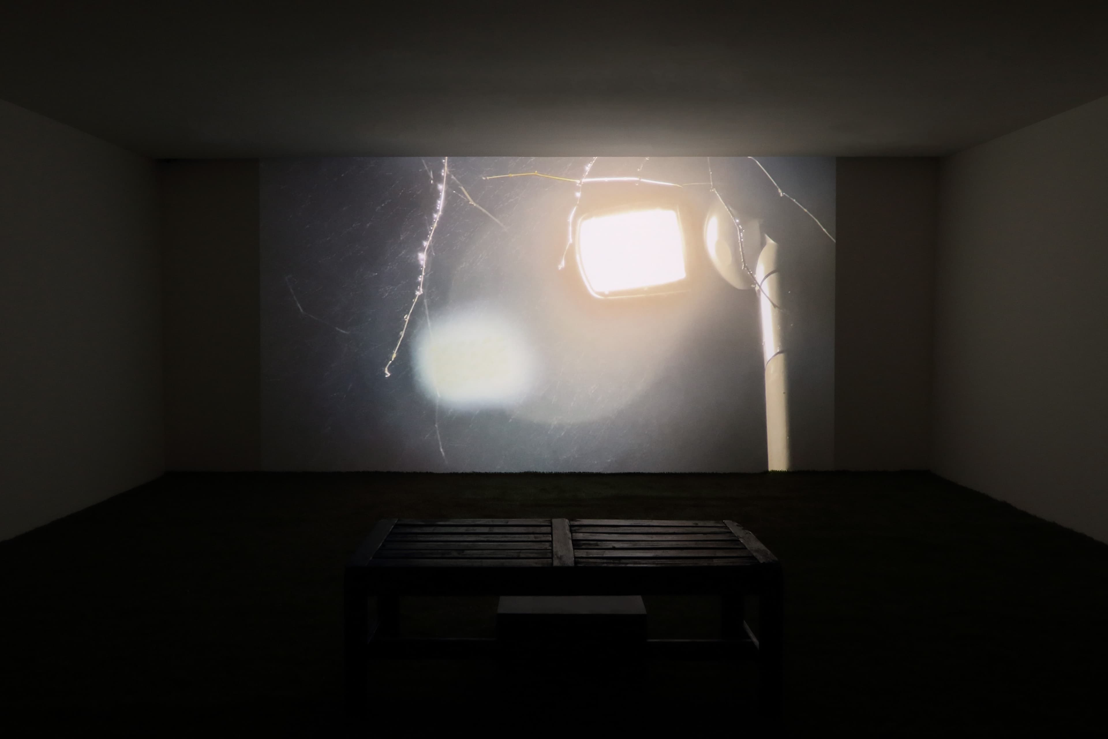 Installation view of a dark room with a large projection of a film by James Prapaithong depicting a streetlight from below