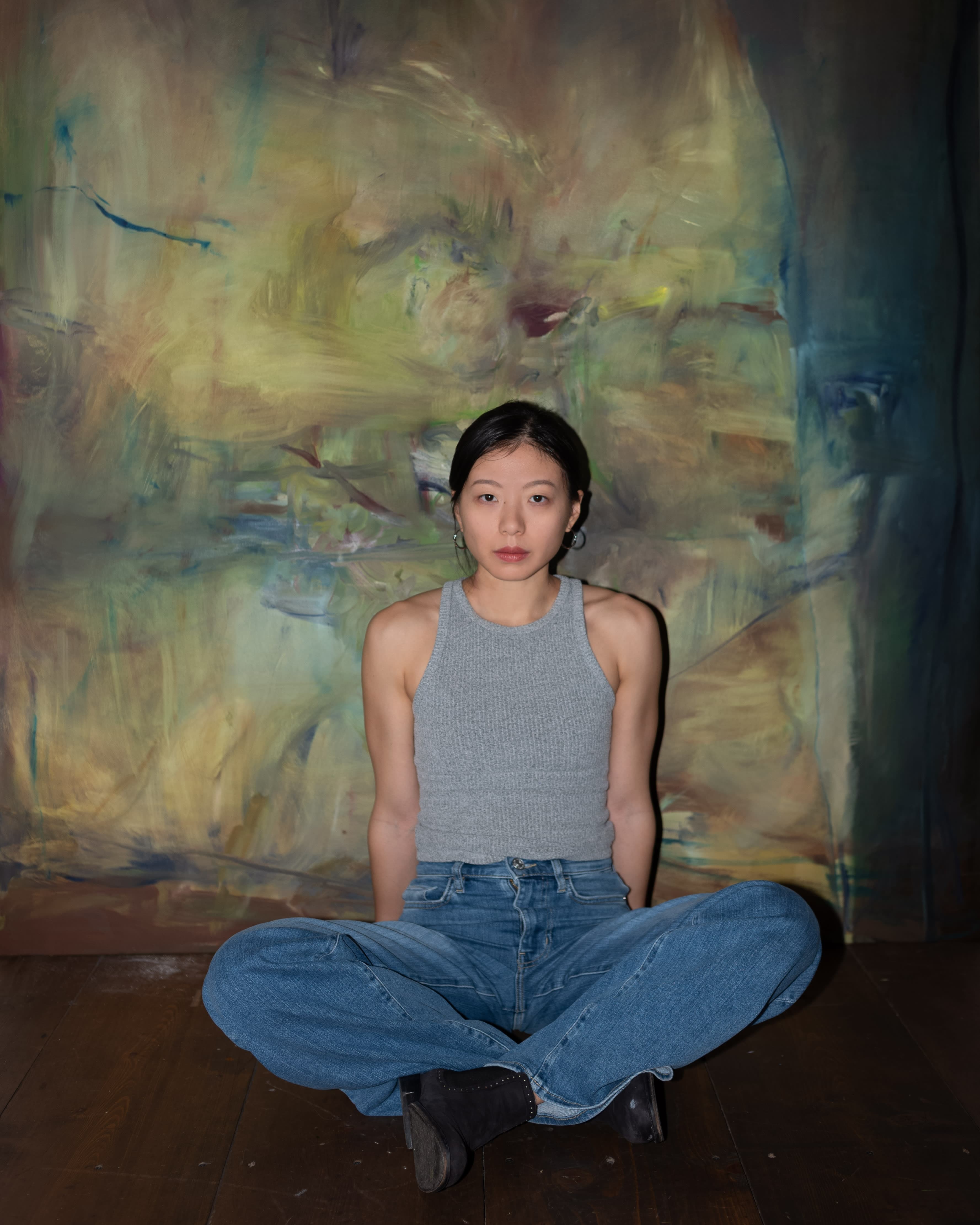 A portrait of Tianyue Zhong sat in front of an abstract painting