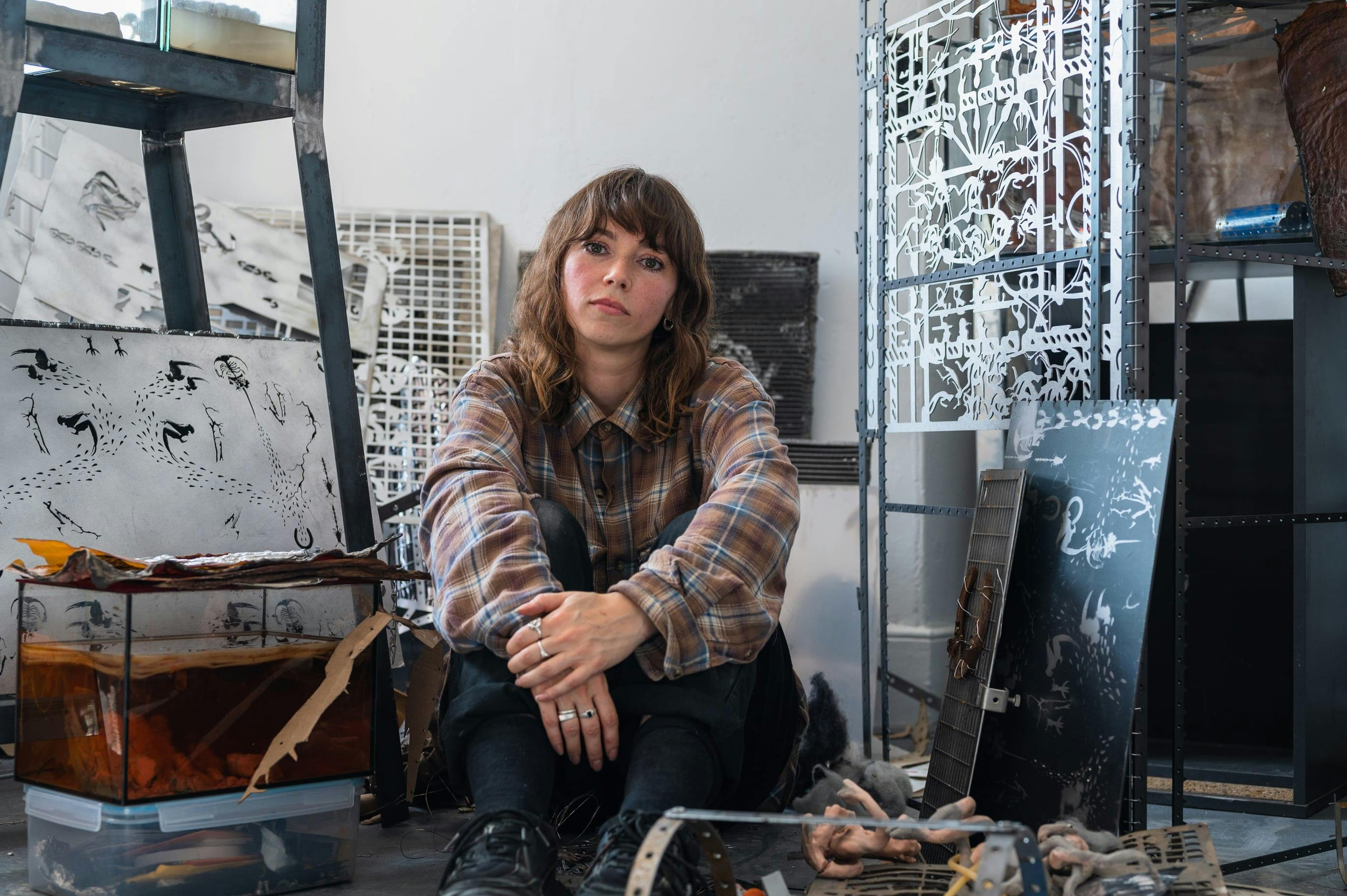 A portrait of Hazel Brill in her studio surrounded by various laser cut steel sheets