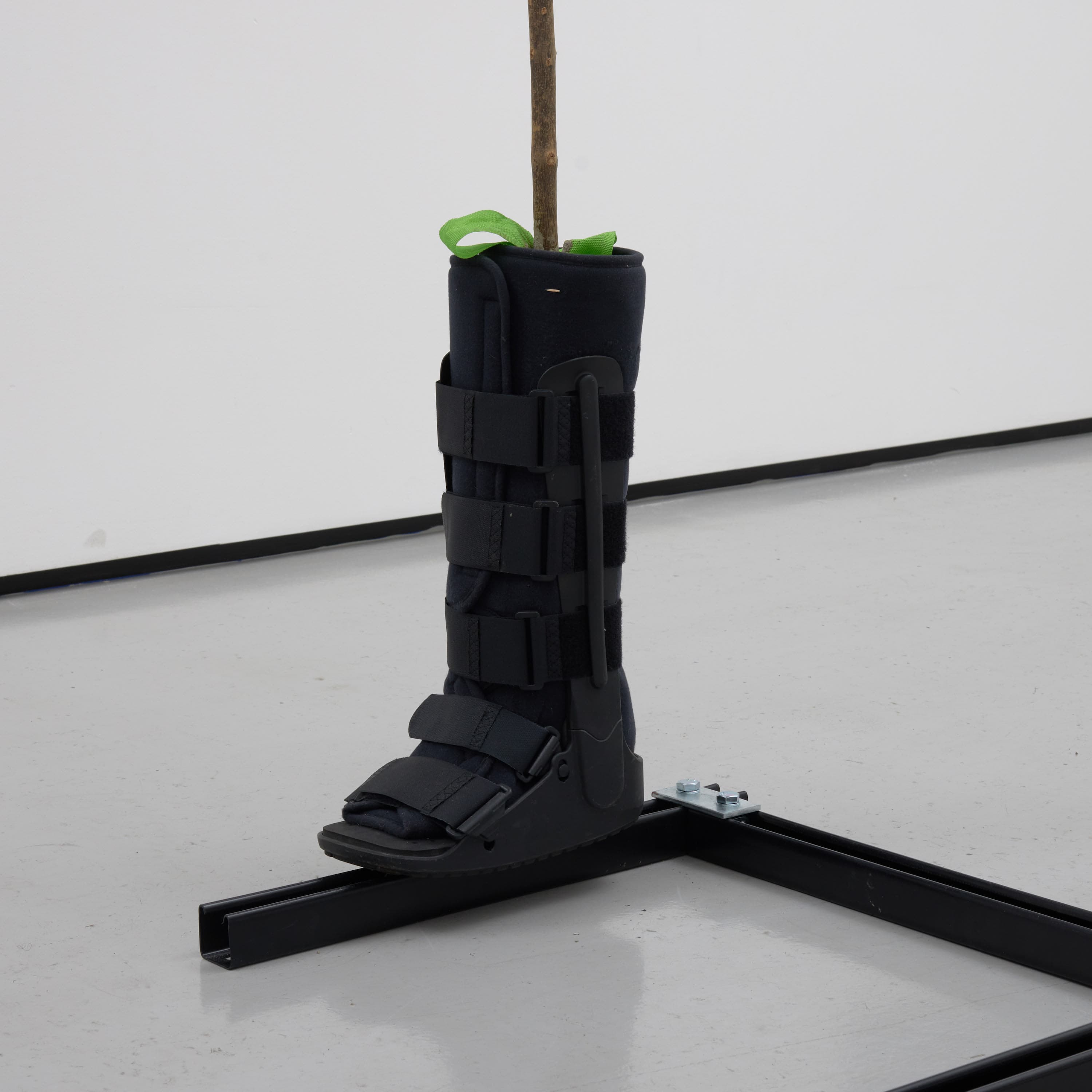 an image of Simeon Barclay's sculpture 'Warrior Falling on Their Feet', 2023 consiting of a Walking stick, umbrella, concrete, betting slip, foot fracture brace walker, bag for life