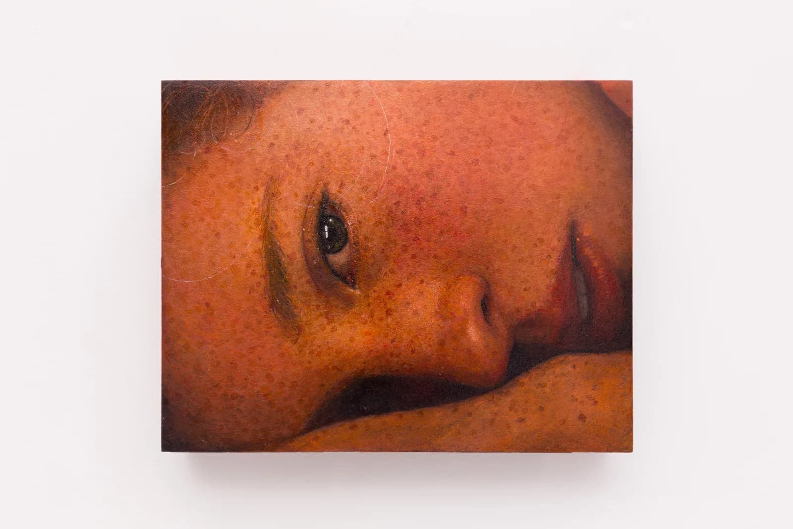 A close-cropped oil on board portrait of a freckled young white woman lying on her side by Ki Yoong