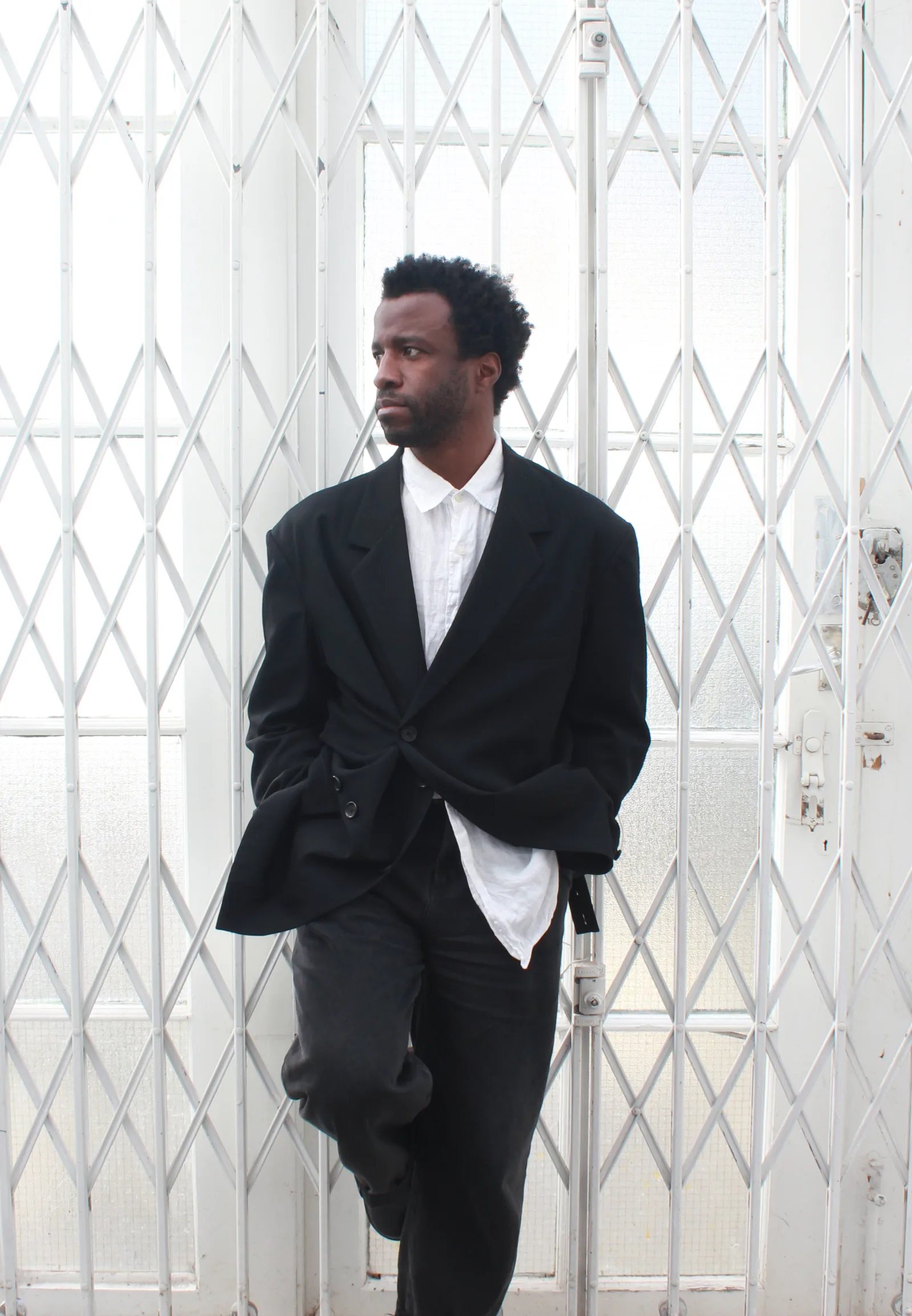 Portraits of artist Simeon Barclay wearing a black suit with white shirt in a minimal semi-industrial setting